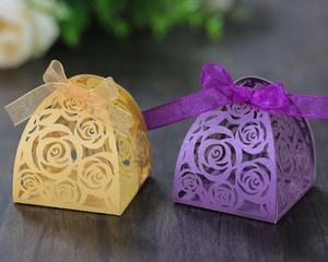 Detailed laser-cut rose hollow candy box with organza ribbon on dark wood surface