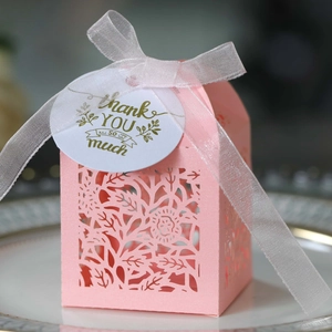 Detail view of pink laser-cut wedding favor box with white ribbon and thank you tag