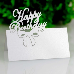 Macro shot of laser-cut white pearlescent Happy Birthday table place card with bow detail