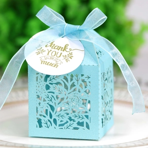 Close-up of laser-cut light blue favor box with floral patterns, ribbon, and thank you tag