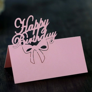 Pink laser-cut Happy Birthday place card with hollow bow design on wood background