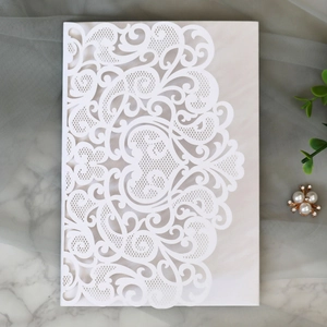 Macro shot of white laser-cut wedding invitation with intricate European scroll patterns