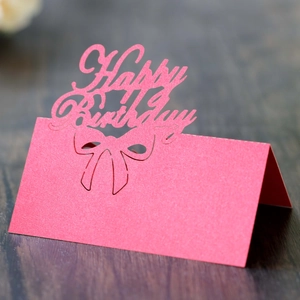 Pink laser-cut Happy Birthday place card with hollow bow design on dark wood background