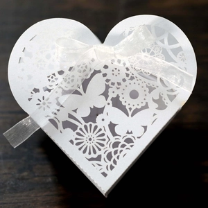 Macro view of white heart-shaped favor box with laser-cut butterfly and floral lace patterns