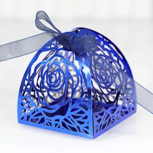 Detail of laser-cut navy blue wedding favor box with rose patterns and ribbon bow