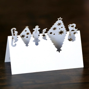 Laser-cut white Christmas table cards with snowflake and reindeer patterns on wood