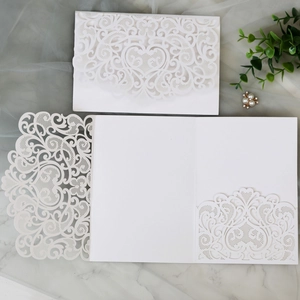 Detail showing white laser-cut wedding invitation set with lace floral heart patterns