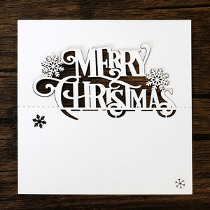 Macro shot of laser-cut white cardstock with Merry Christmas text and snowflake details