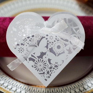 Close-up of laser-cut white heart favor box with butterfly pattern and silk ribbon
