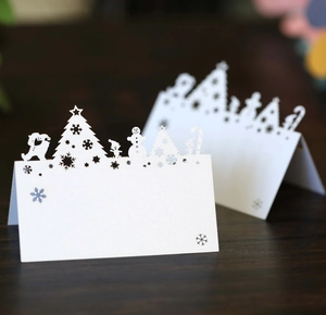 White laser-cut Christmas place cards featuring reindeer and tree designs on wood table