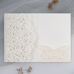 Detail of laser-cut cream pearl paper wedding invitation with floral lace patterns