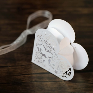 Macro shot of white laser-cut butterfly heart wedding candy box on dark wood surface