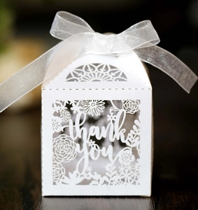 Detail of white laser-cut 'Thank You' wedding favor box with ribbon on wooden table