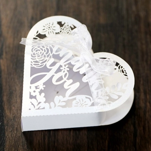 Detail of white heart-shaped favor box with laser-cut floral patterns and Thank You text