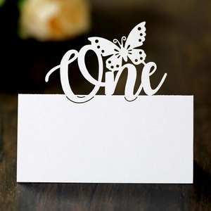 Detail of laser-cut white butterfly card with One text on a warm wooden surface