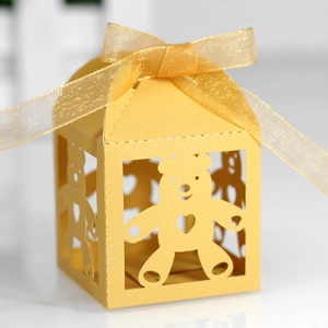 Detail of yellow laser-cut candy box featuring a hollow bear design and golden ribbon