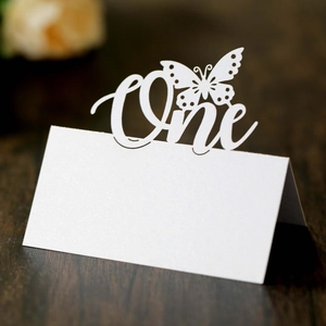 Laser-cut butterfly place card with One lettering on a dark wood background table