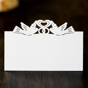Laser cut heart and lovebirds wedding place cards in white textured paper on wood surface