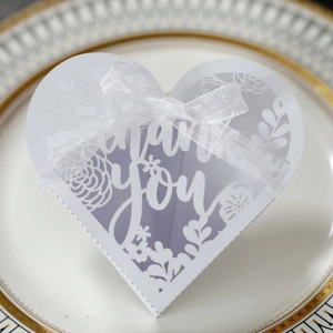 Detail showing laser-cut 'thank you' text on white heart-shaped favor box with ribbon