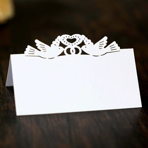 Detail of laser-cut wedding place card featuring white paper doves, heart and rings