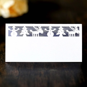Detail of white laser-cut Christmas place card with snowman and reindeer on wood table