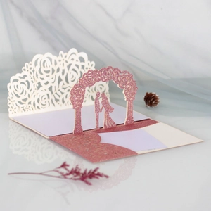 Detail of 3D pop-up wedding card with laser-cut pink glitter floral arch and couple