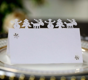 White laser-cut Christmas place cards with snowman and reindeer designs for table settings
