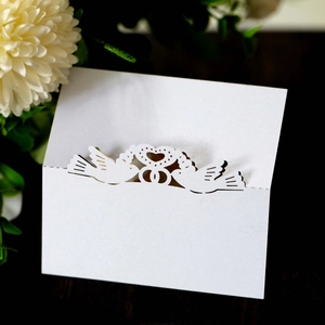 Detail of white laser-cut seat card with love birds heart design and pearlescent finish