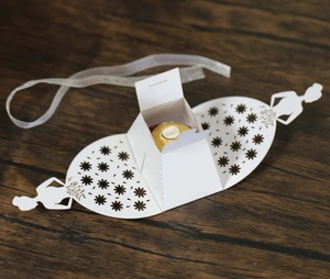 Macro detail of bridal dress shaped white laser-cut favor box with silk ribbon and floral pattern