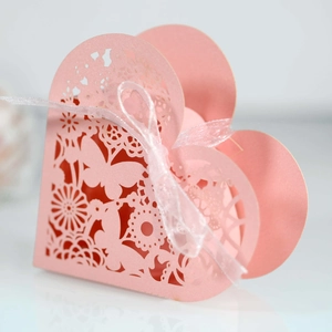 Macro shot of laser-cut butterfly patterns on a pink heart candy box with white ribbon