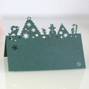 Close-up of laser-cut Christmas tree and snowman on dark green table place card