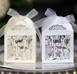 Detail of laser-cut ivory floral favor boxes with 'thank you' text and organza ribbon