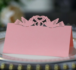 Detail of pink laser-cut place card with bird and heart motif on elegant plate