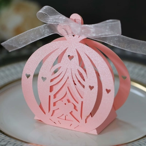 Macro view of pink laser-cut carriage favor box with a white ribbon on a ceramic plate