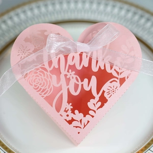 Detail of pink heart-shaped laser cut favor box with thank you text and white ribbon