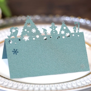 Macro detail of laser-cut teal Christmas place card with snowflake and tree patterns