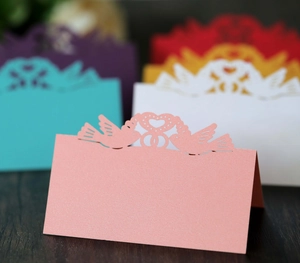 Detailed laser-cut pearl paper table card with heart and bird design for weddings