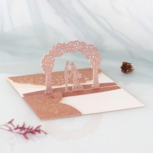 Detail of rose gold 3D pop-up wedding invitation featuring laser-cut floral arch and couple