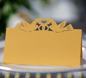 Detailed laser-cut wedding table card with hollow heart and dove design on golden paper