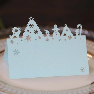Laser-cut light blue Christmas place card with snowman and tree on white ceramic plate