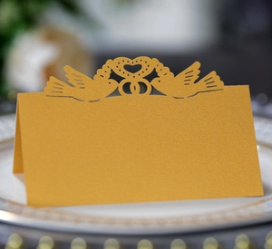 Macro view of a laser-cut gold wedding place card with heart and bird motifs on a plate