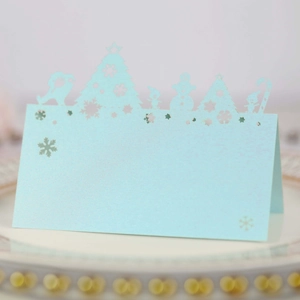 Macro shot of laser-cut light blue Christmas place card with snowman and tree pattern