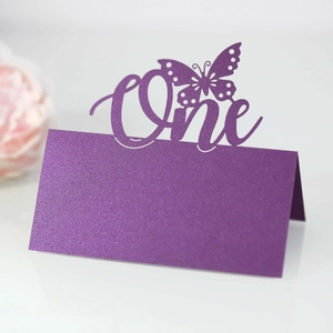 Macro detail of purple glitter seat card featuring laser-cut butterfly and One lettering