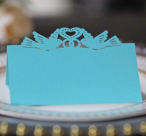 Close-up of light blue laser-cut place card with pigeons and heart on a dinner plate