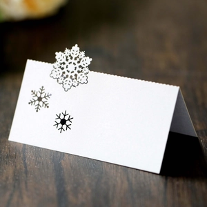 Detail of laser-cut snowflake on white paper place card over dark wood table surface