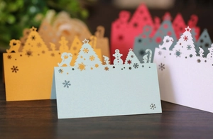 Laser-cut Christmas place cards featuring holiday trees and snowmen on wood surface
