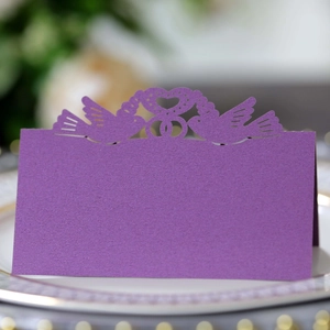Detail of laser-cut purple heart and birds table card on a white dinner plate