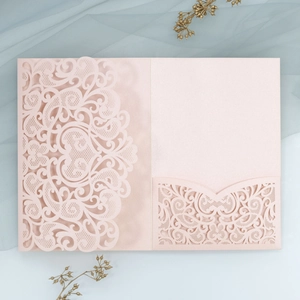 Macro view of laser-cut lace floral pattern on champagne pink wedding invitation card