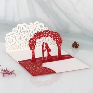 Macro detail of laser-cut 3D wedding card with glitter red couple under rose arch