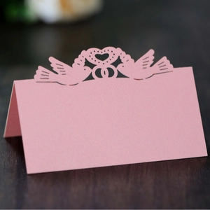Pink laser-cut wedding place cards with heart and bird design on wooden table